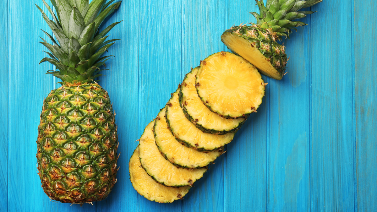 Slices of ripe pineapple and whole fruit on wooden background
